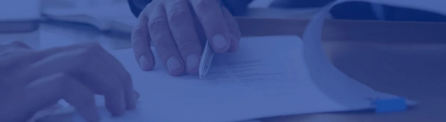 A person's hand signing a document on a desk with a pen.